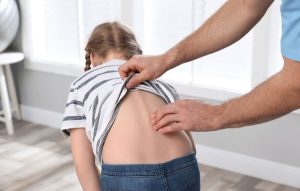 Child bending down while doctor examines her spine