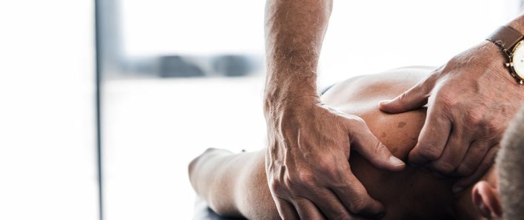 Close up of a person laying on the massage table with the therapist massaging the shoulder.