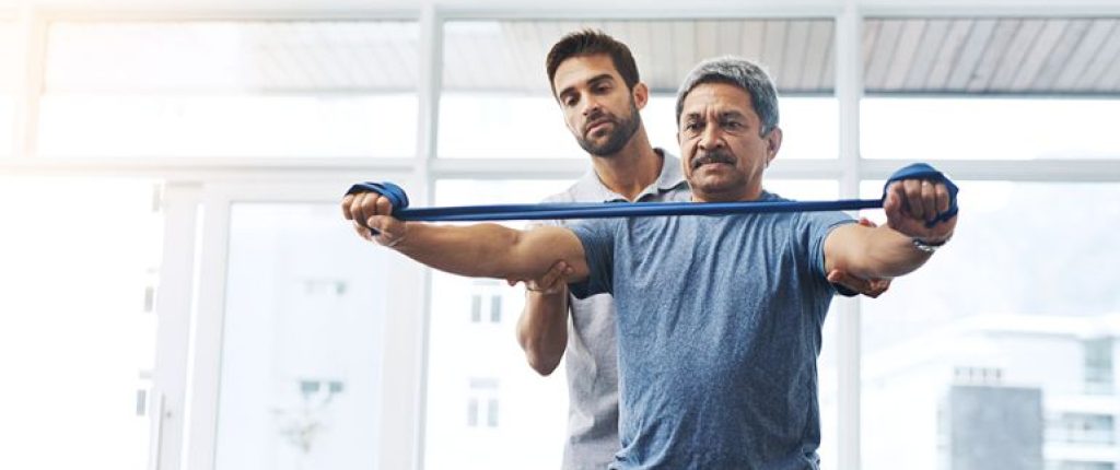 Older man working with an physical therapist to train with arm bands