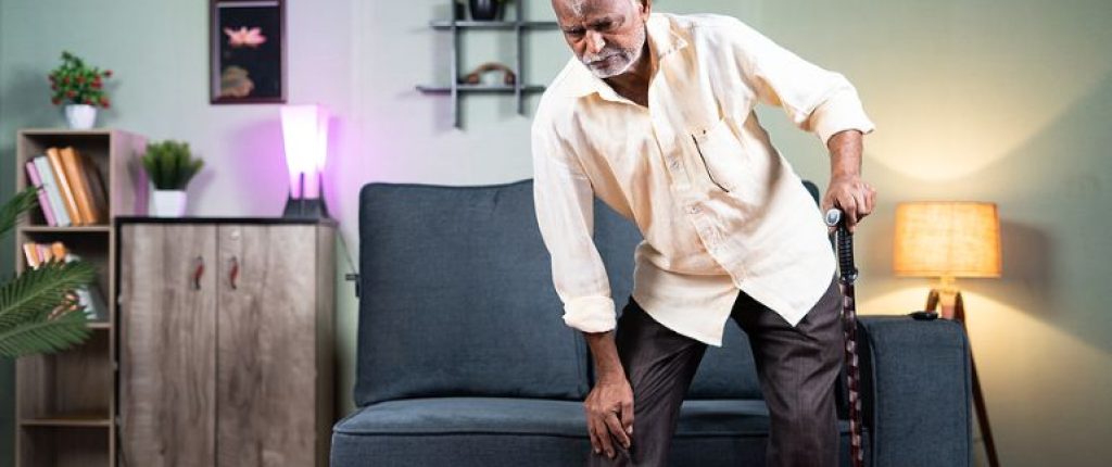 Man standing up and holding his knee as if he's in pain.