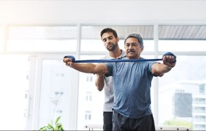Older man working with an physical therapist to train with arm bands
